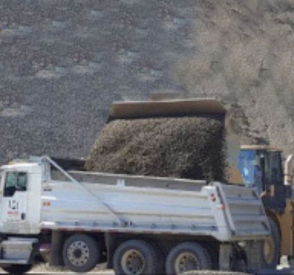 Truck dumping rocks into the back of another truck